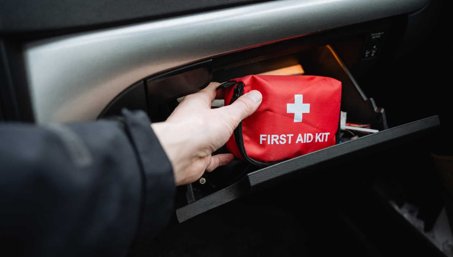 Driver placing a compact first-aid kit in the glovebox before a UK winter journey
