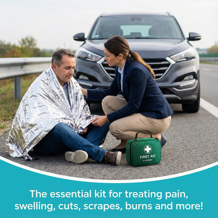 Person wrapped in a blanket with another person attending to them next to a car on the side of the road, with a first aid kit visible.