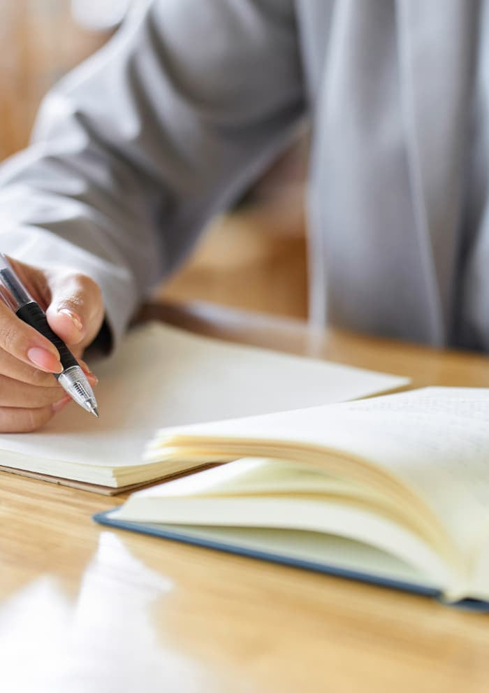 Person writing in a notebook about first aid kits certification with a pen on a wooden table