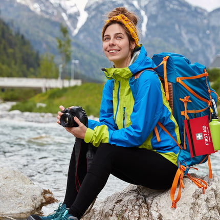 Person with a backpack and camera sitting by a river with mountains in the background