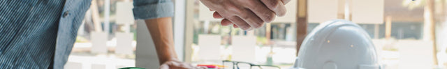 Two people shaking hands with a green first aid kit on a table in an office setting.